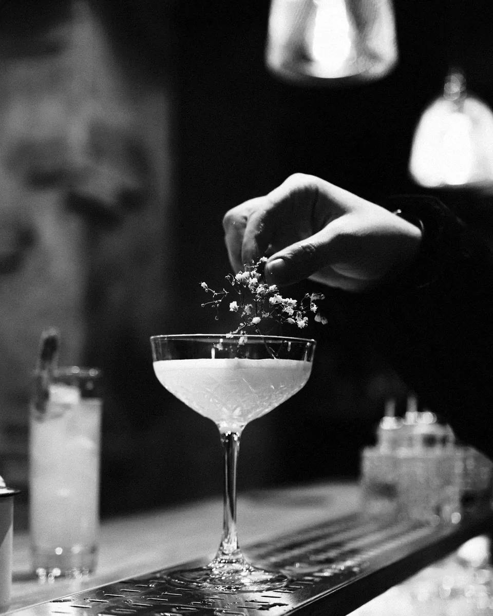 A bartender finishes a coupe with a garnish at the bar.