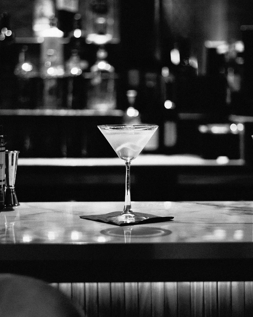 A single martini waits on a long marble bar.