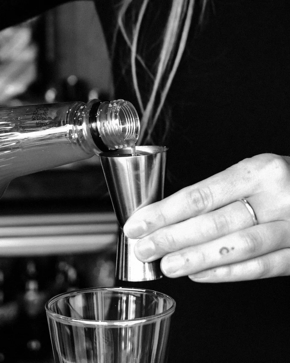 A bartender measures a pour with a steel jigger.