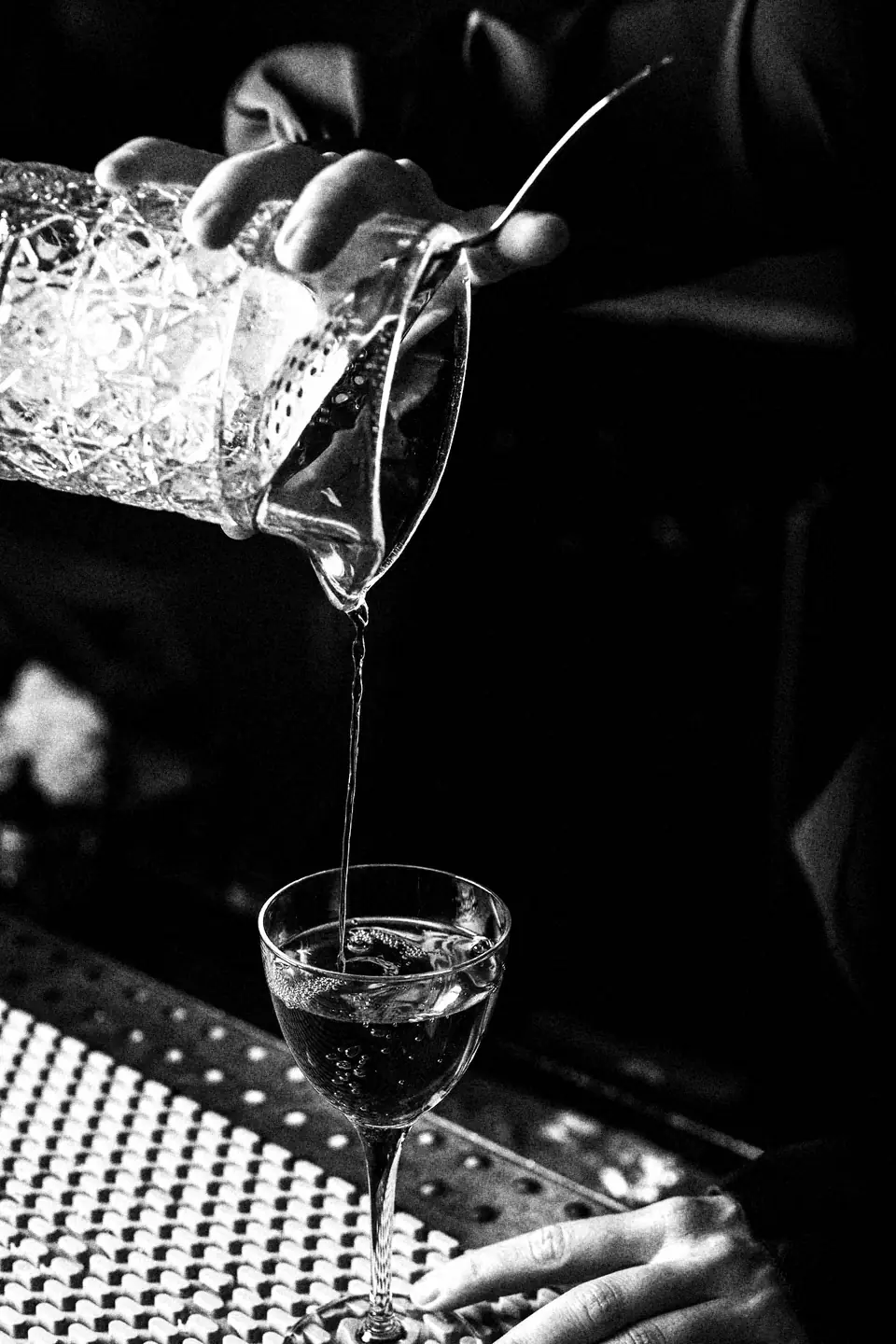 A bartender strains a stirred cocktail from a crystal mixing glass into a coupe.