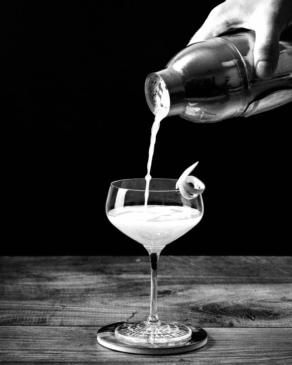 A shaken cocktail poured into a coupe with a citrus twist.