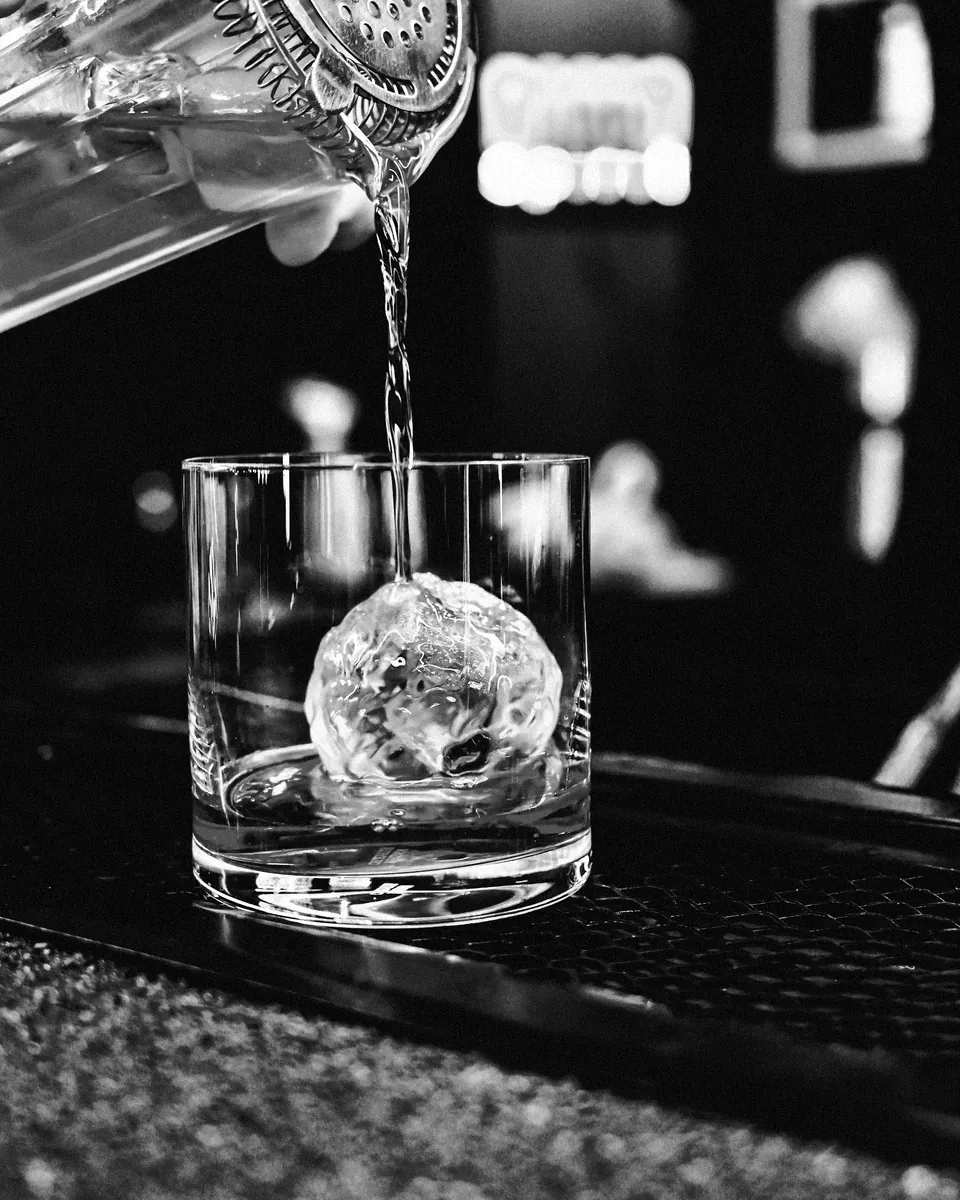 A drink poured over a clear ice sphere.