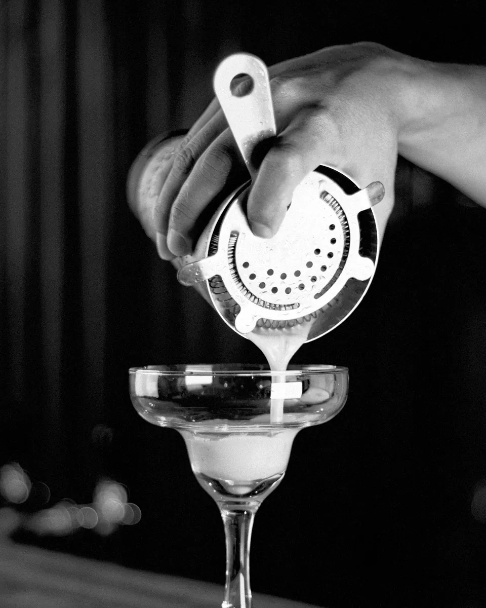 A cocktail strained through a hawthorne strainer into a coupe.