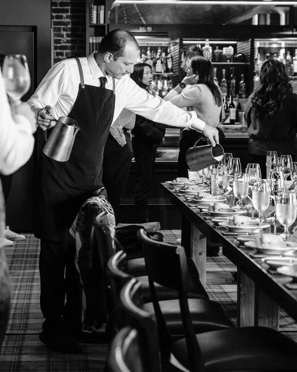 A server pours down a long dinner table set for a party.