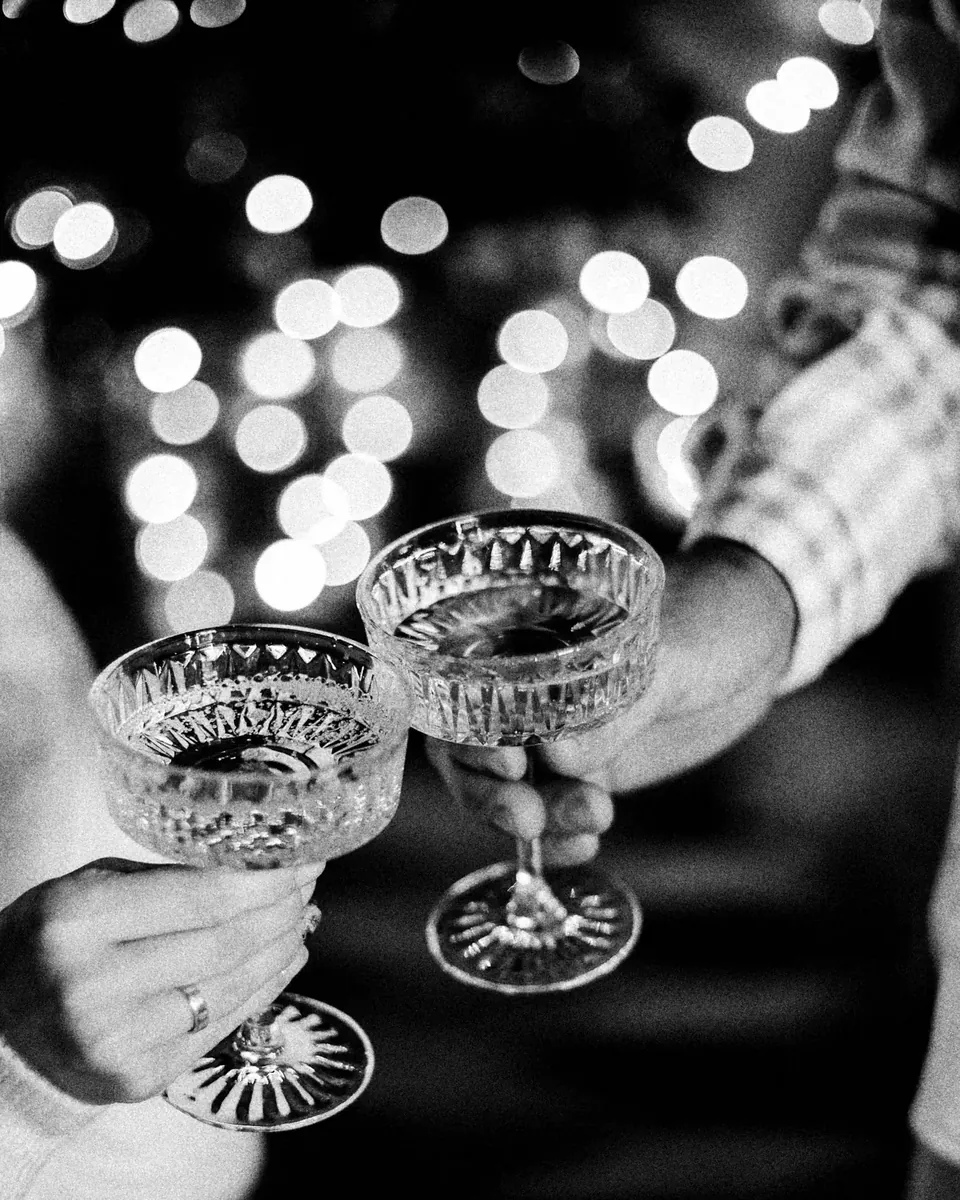 Two guests touch crystal coupes under string lights.