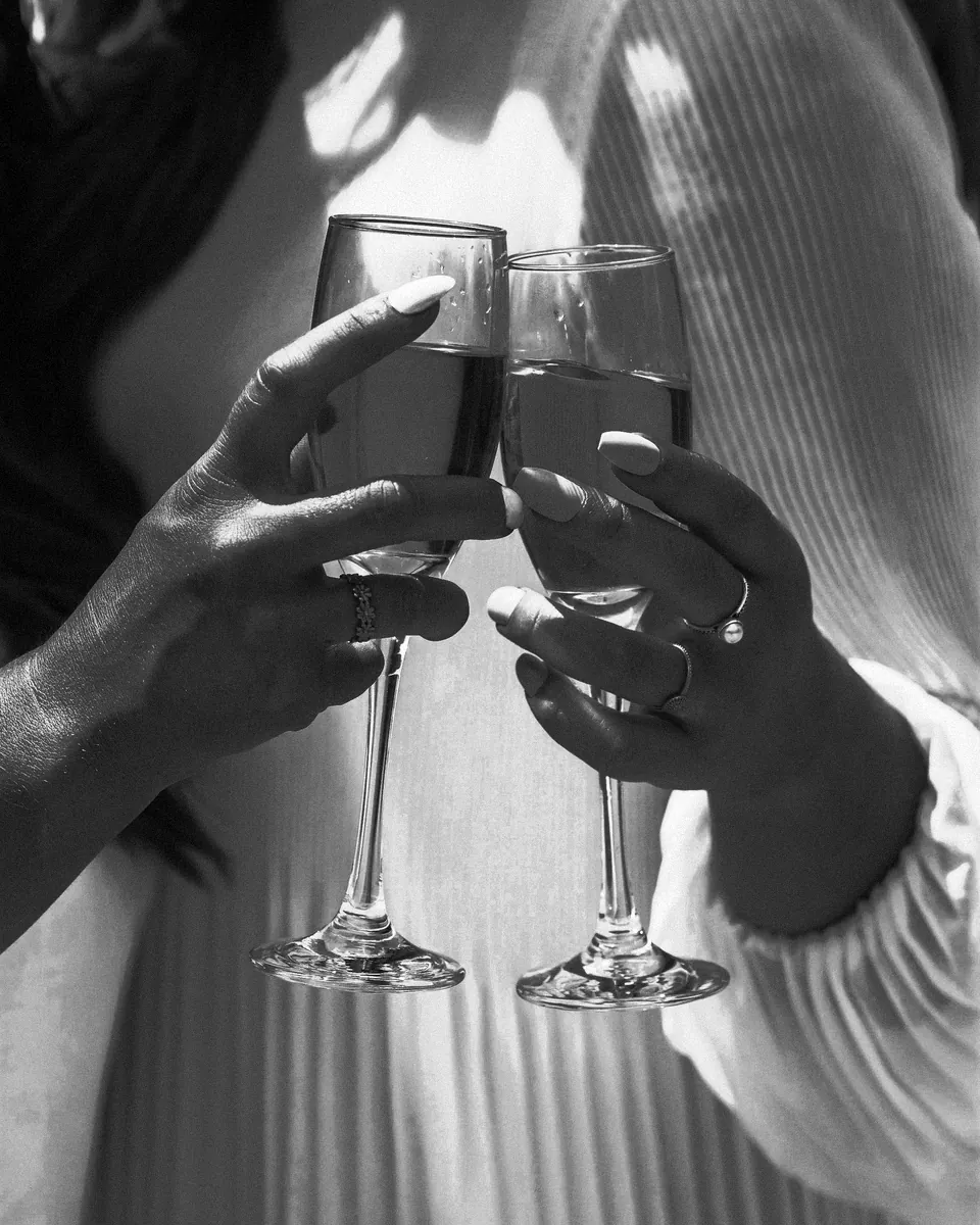 Two hands hold champagne flutes at a wedding.
